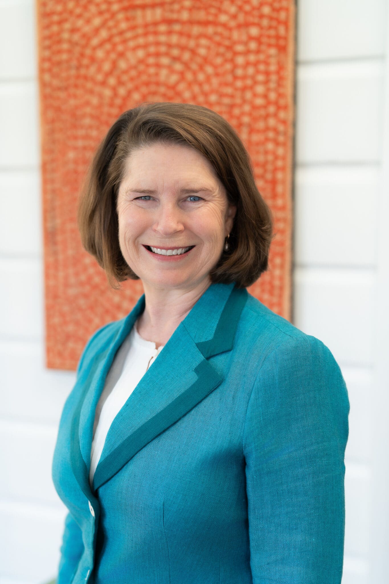Female CEO in a blue jacket standing in front of an orange painting having her headshot taken by professional photographer Georgie Greene