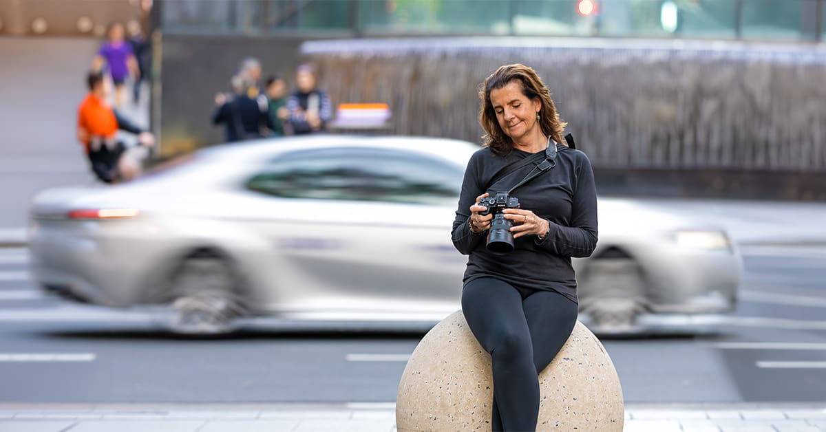 Georgie Greene Sydney photographer sitting on a stone ball looking at her camera
