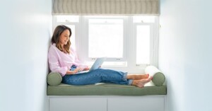 dark haired marketing specialist sitting on a green window seat typing at her computer having her personal branding photo taken by professional Sydney photographer Georgie Greene