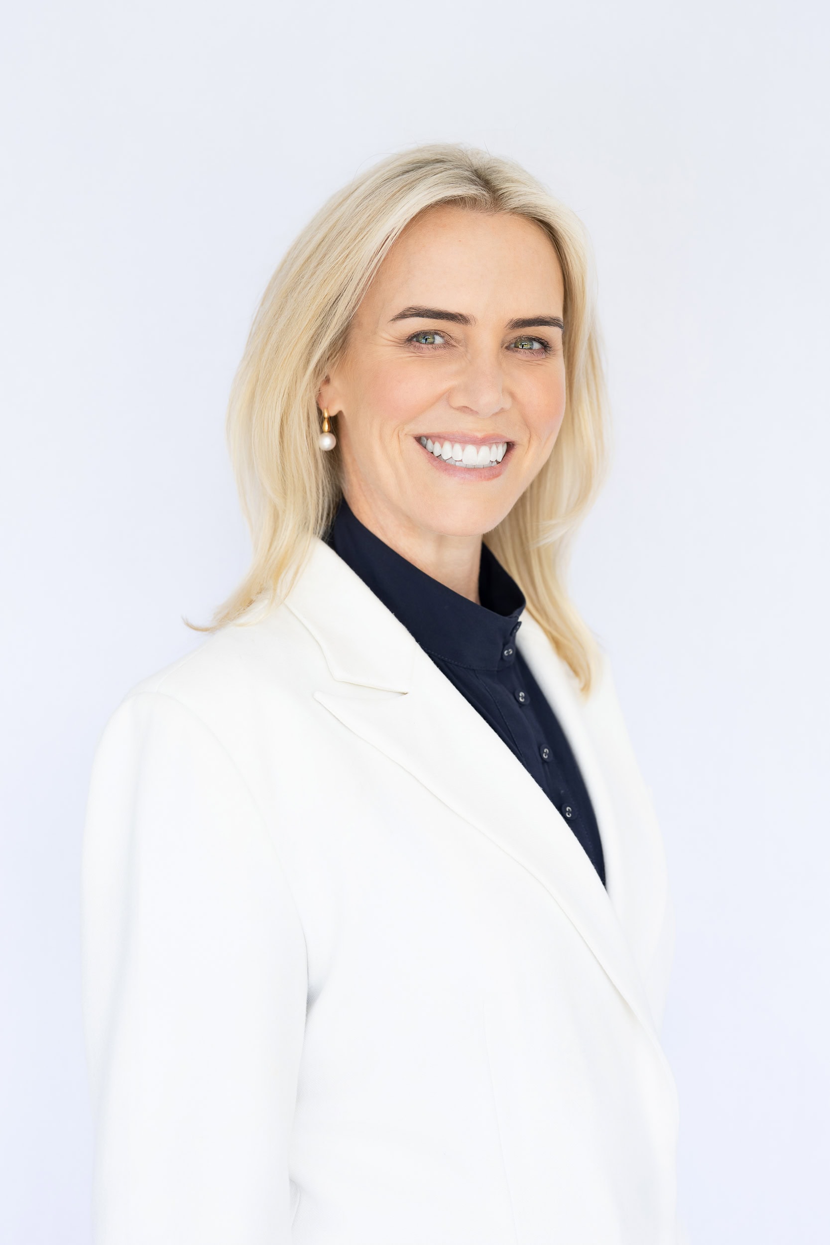 smiling blond woman wearing a white jacket while she has a mini-branding headshot taken by Georgie Greene